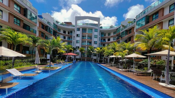 A modern hotel with a central swimming pool, multiple balconies, and outdoor seating areas. - Miramar Luxor Paulo Miranda - C. Branco (João Pessoa)