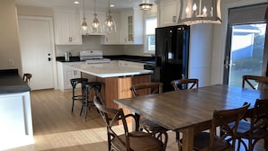 Una cocina moderna con armarios blancos, un refrigerador negro, una mesa de comedor de madera y taburetes de bar.