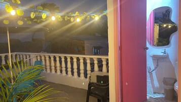 A balcony with string lights, a chair, and a potted plant.
