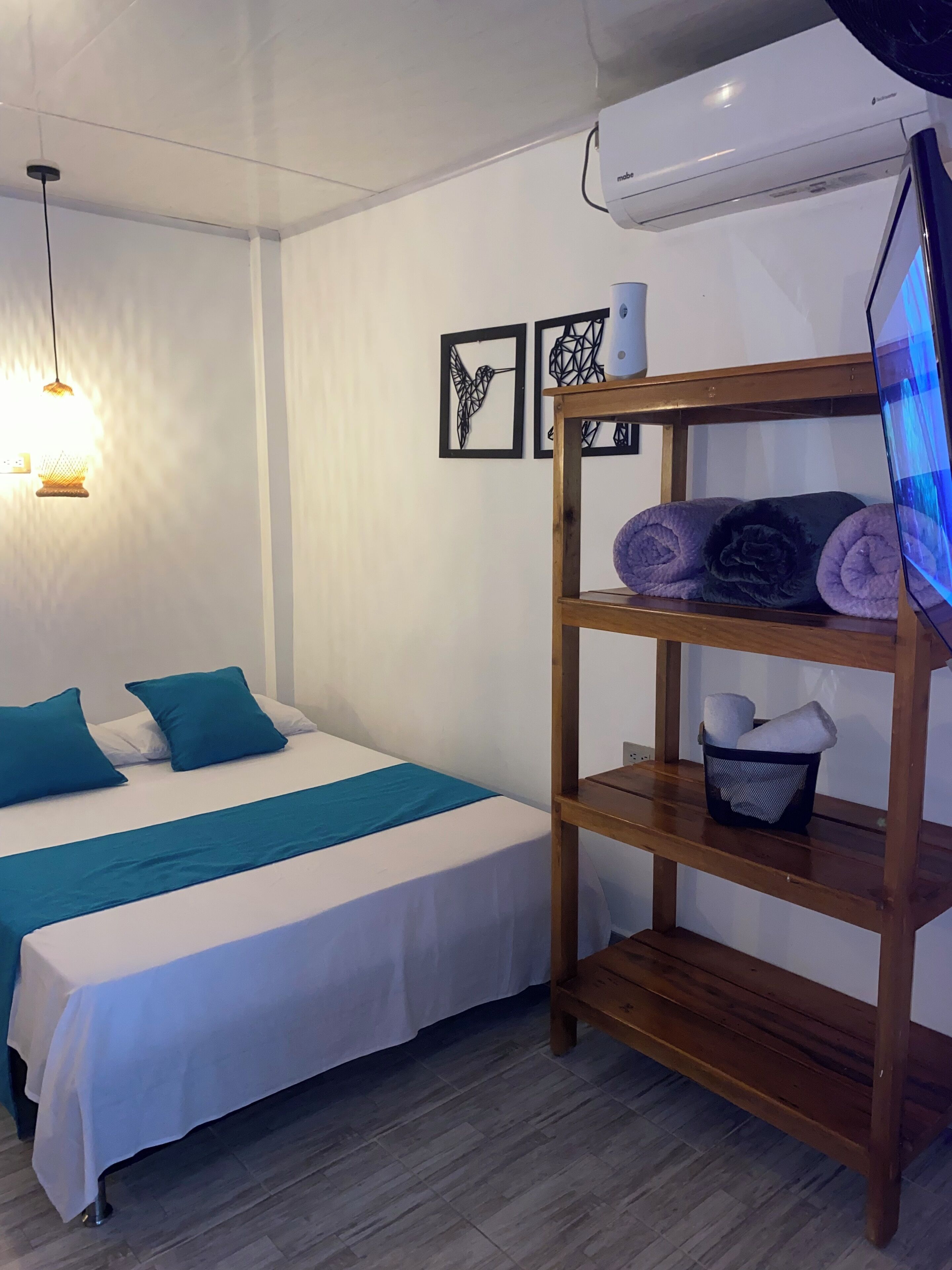 Un dormitorio ordenado con cama, estante de madera con toallas, decoración en la pared y equipo de aire acondicionado.