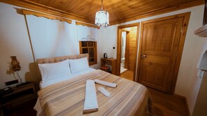A bedroom with a large bed, wooden ceiling, a chandelier, a nightstand, a small table, and a wardrobe. - Utku Konağı (Bartin)