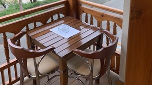 A wooden balcony with a table and chairs, overlooking a river and greenery.