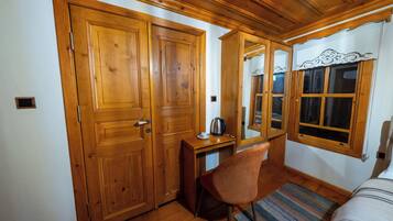 Una habitación con puertas de madera, un escritorio con una silla, una cama y una ventana con cortinas.