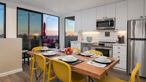 A modern kitchen with white cabinets, stainless steel appliances, and a dining area with yellow chairs and a wooden table set for four. - 4 Bed Penthouse w/City View Deck and Firepit. Near Zoo (San Diego)
