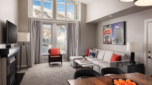 Ein modernes Wohnzimmer mit einer Couch, Sesseln, einem Esstisch mit Orangen, einem Fernseher und einem Gemälde an der Wand.