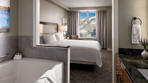 Ein Hotelzimmer mit einem großen Bett, einem separaten Badezimmer mit Badewanne, einem Fenster mit Blick auf die Berge und einer Marmorplatte.