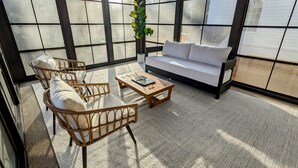 A sunlit room with a sofa, two wicker chairs, a coffee table, and a potted plant.