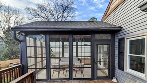 A covered patio with a wooden deck, a seating area with chairs and a table, and a view of the backyard.