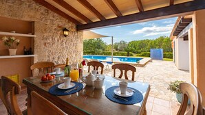Ein Essbereich mit einem für das Frühstück gedeckten Tisch, mit Blick auf einen Swimmingpool und üppiges Grün.