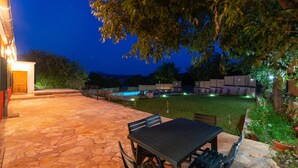 Un patio al aire libre con suelo de piedra, una mesa y sillas, y una piscina de fondo.