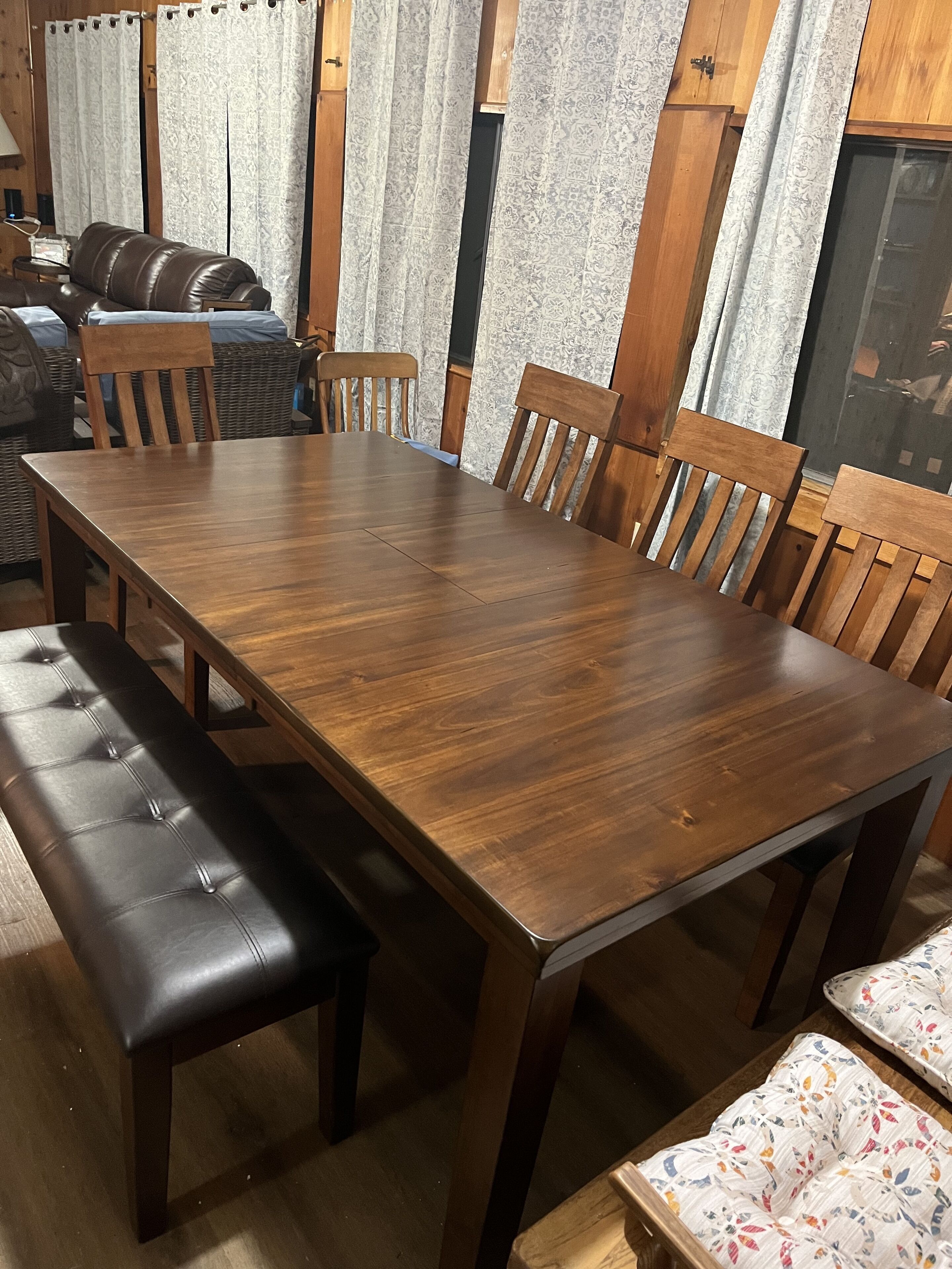 Een houten eettafel met zes stoelen, een bank en gordijnen met een patroon.
