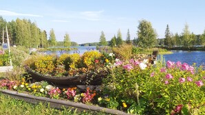 Puutarha, jossa on kukkia täynnä oleva puuvene, järvi ja taustalla näkyviä puita.
