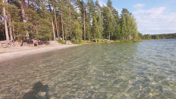 Kirkasvetinen järvi, jossa on hiekkaranta ja tiheä metsä.