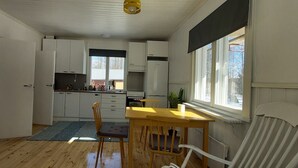 Kompakti keittiö, jossa on valkoiset kaapit, ruokapöytä ja tuoli. Keittiössä on ikkuna, josta tulee luonnonvaloa.