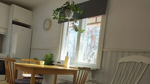 Ruokailutila, jossa on puinen pöytä ja tuolit, riippuvassa ruukussa oleva kasvi ja ikkuna, josta avautuu näkymä puihin.