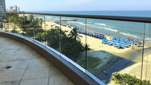 A balcony with a view of a beach with blue umbrellas and palm trees. - Apartamento Palmetto Eliptic Ocean View (Cartagena)