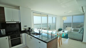 A modern kitchen with a central island, a dining area with a glass table, and a view of the ocean through large windows. - Apartamento Palmetto Eliptic Ocean View (Cartagena)