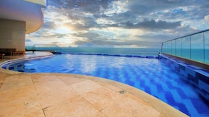 A swimming pool with a view of the ocean, a curved building, and a glass railing. - Apartamento Palmetto Eliptic Ocean View (Cartagena)