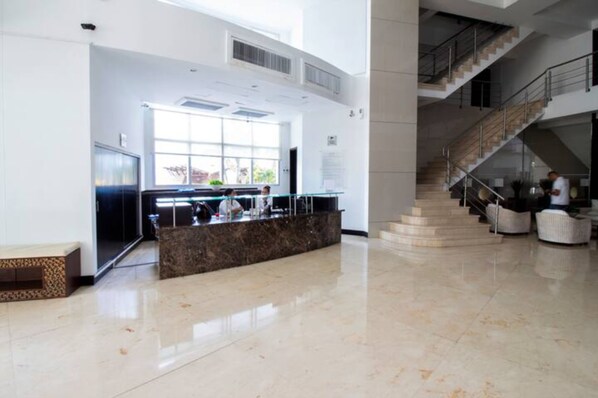 A spacious lobby with a marble floor, a reception desk, and a staircase leading to upper levels.