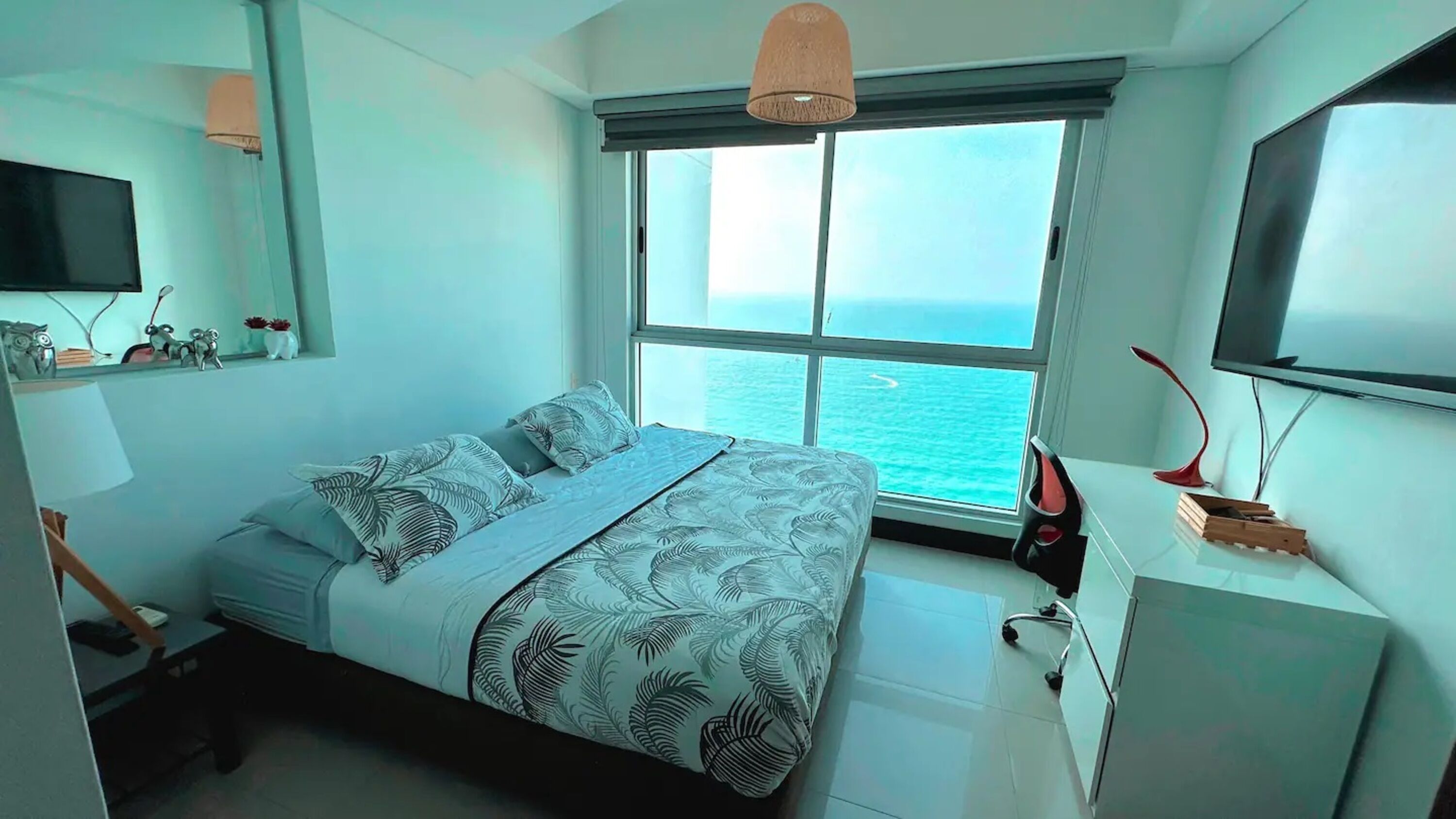 Un dormitorio moderno con una cama grande, un televisor, un escritorio y vista al océano.