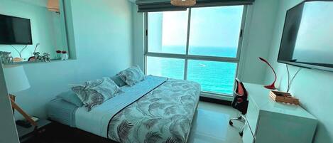 Un dormitorio moderno con una cama grande, un televisor, un escritorio y vista al océano.