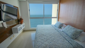 A bedroom with a large bed, a TV mounted on the wall, and a view of the sea through a large window. - Apartamento Palmetto Eliptic Ocean View (Cartagena)