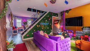Una sala de estar vibrante con un sofá morado, una escalera con plantas verdes y un televisor en la pared.