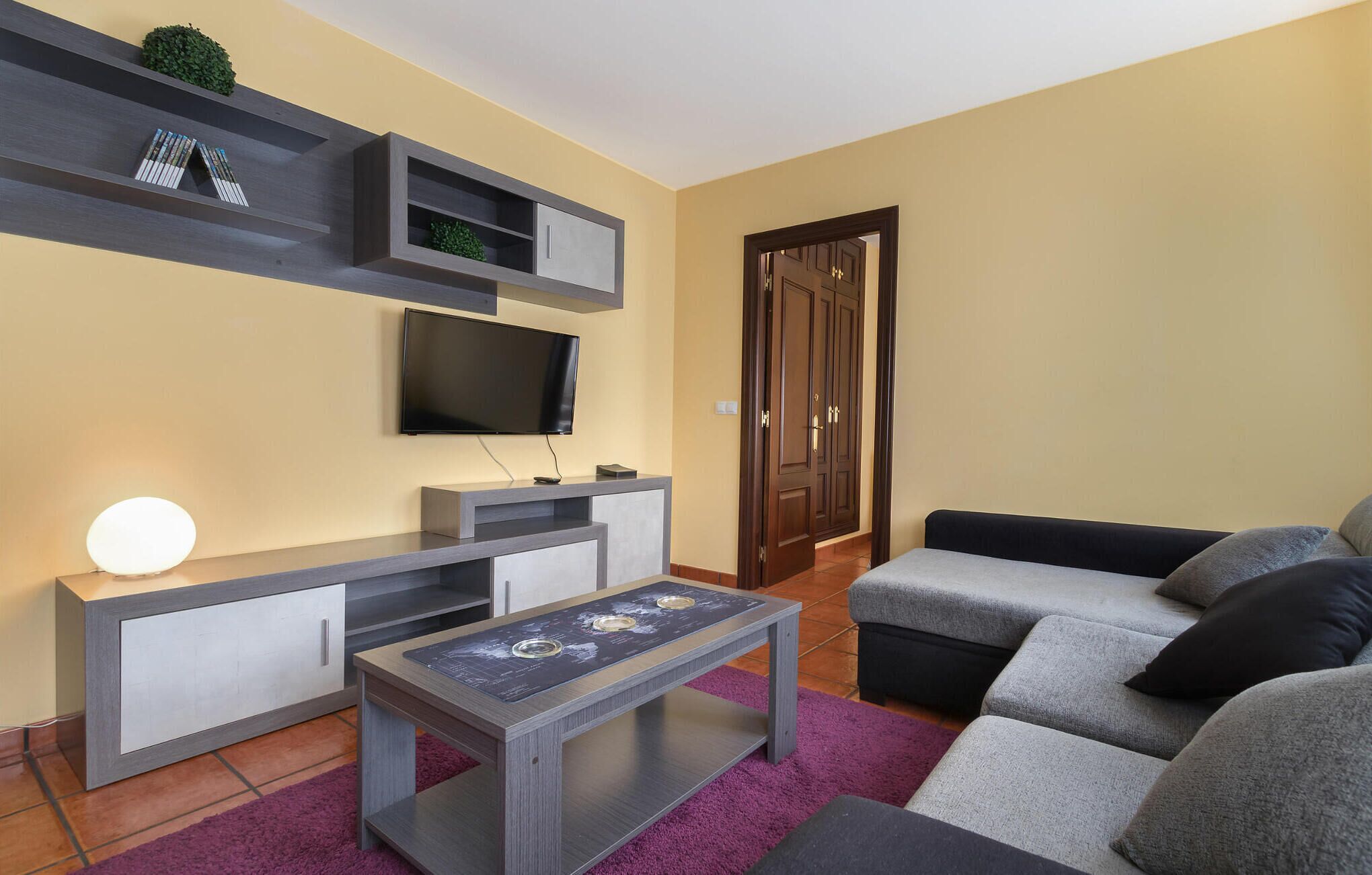 Ein Wohnzimmer mit Flachbildfernseher an der Wand, einem Couchtisch, einer Couch und einem Bücherregal.