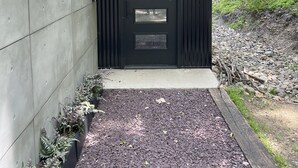 Een modern gebouw met een zwarte deur, een betonnen muur en een grindpad dat naar de ingang leidt.
