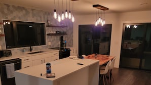 Een moderne keuken met een centraal eiland, houten vloeren en hangende lampen.