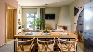 Een moderne eethoek met een houten tafel en stoelen, een televisie aan de muur en een keuken met een koelkast.