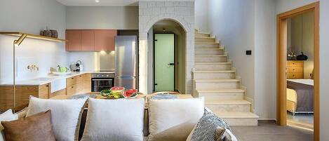 Un interior moderno con una cocina, una escalera y una sala de estar con sofá y cojines.
