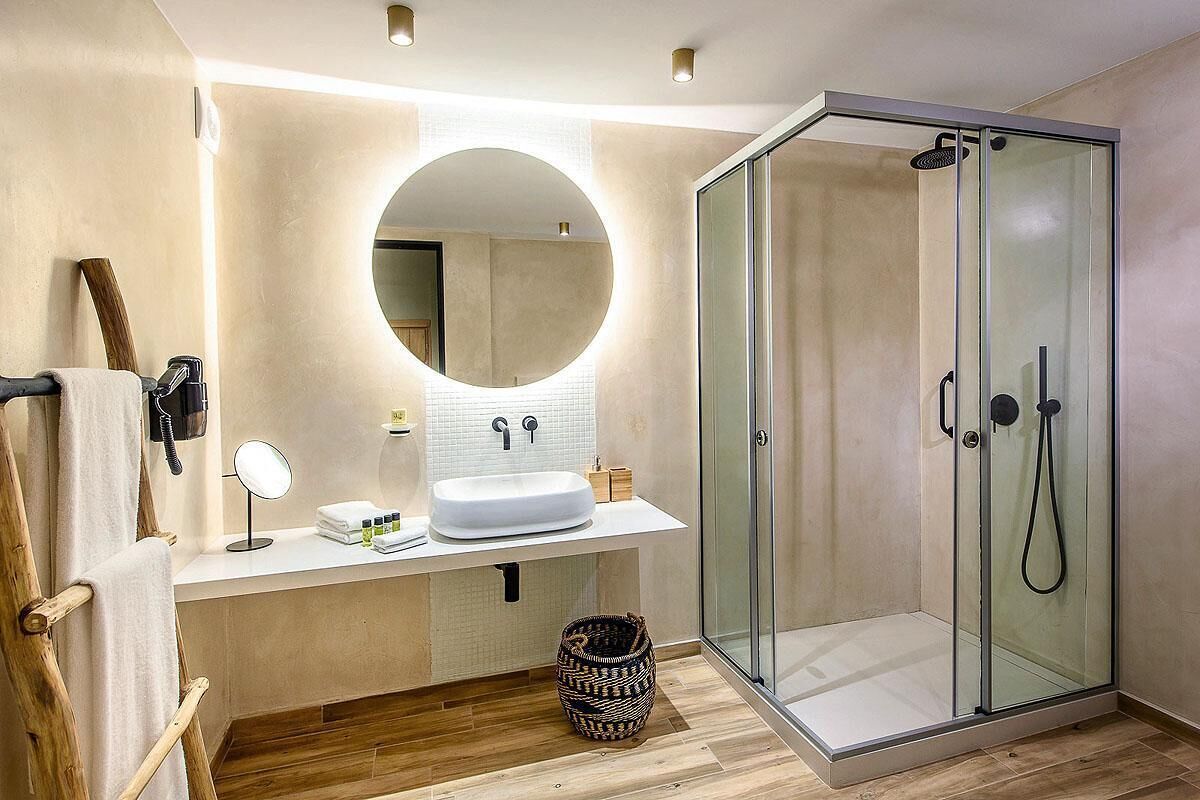 Ein modernes Badezimmer mit einer gläsernen Duschkabine, einem runden Spiegel über einem Waschbecken und Holzboden.