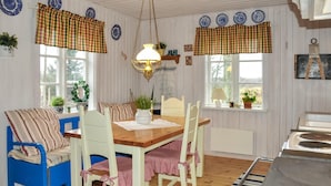 Un coin repas accueillant avec une table et des chaises en bois, un luminaire suspendu et une fenêtre agrémentée d’un rideau à carreaux.
