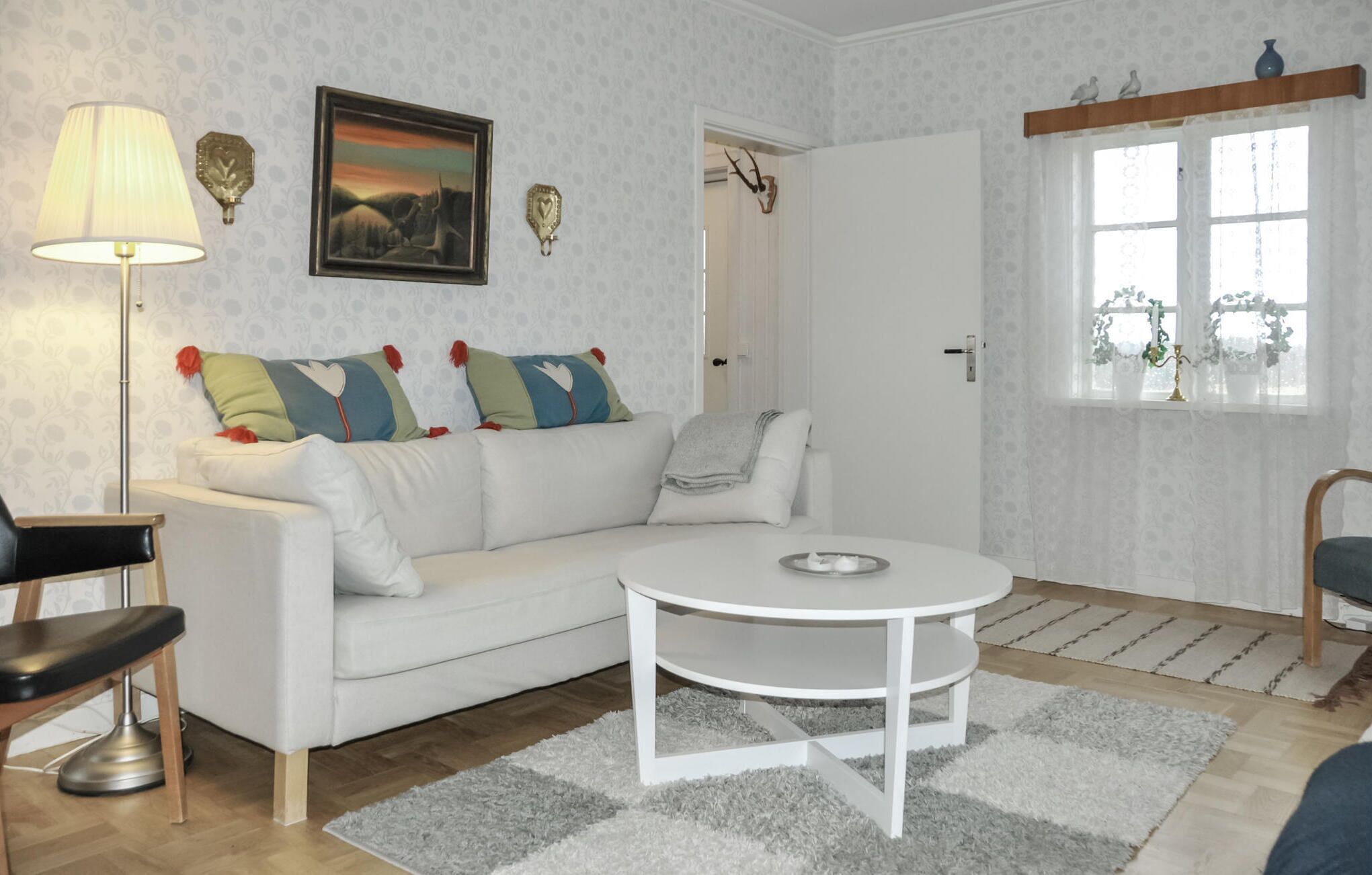 Un salon moderne avec un canapé blanc, une table basse ronde, une lampe et un tableau accroché au mur.