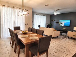 A modern living room with a flat-screen TV, a sofa, and a dining area with a wooden table and chairs.
