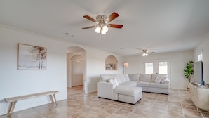 A spacious living room with a sectional sofa, a ceiling fan, and a bench.