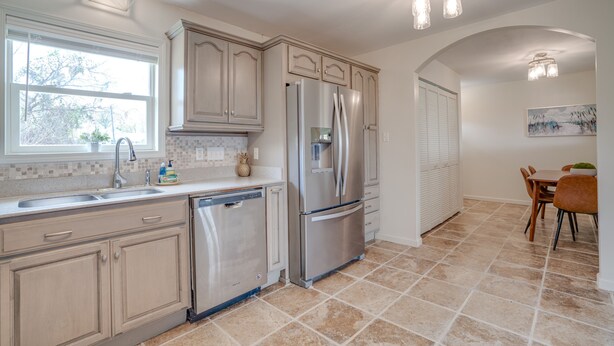 A kitchen with a stainless steel refrigerator, dishwasher, and double sink. There is a dining area with a table and chairs.