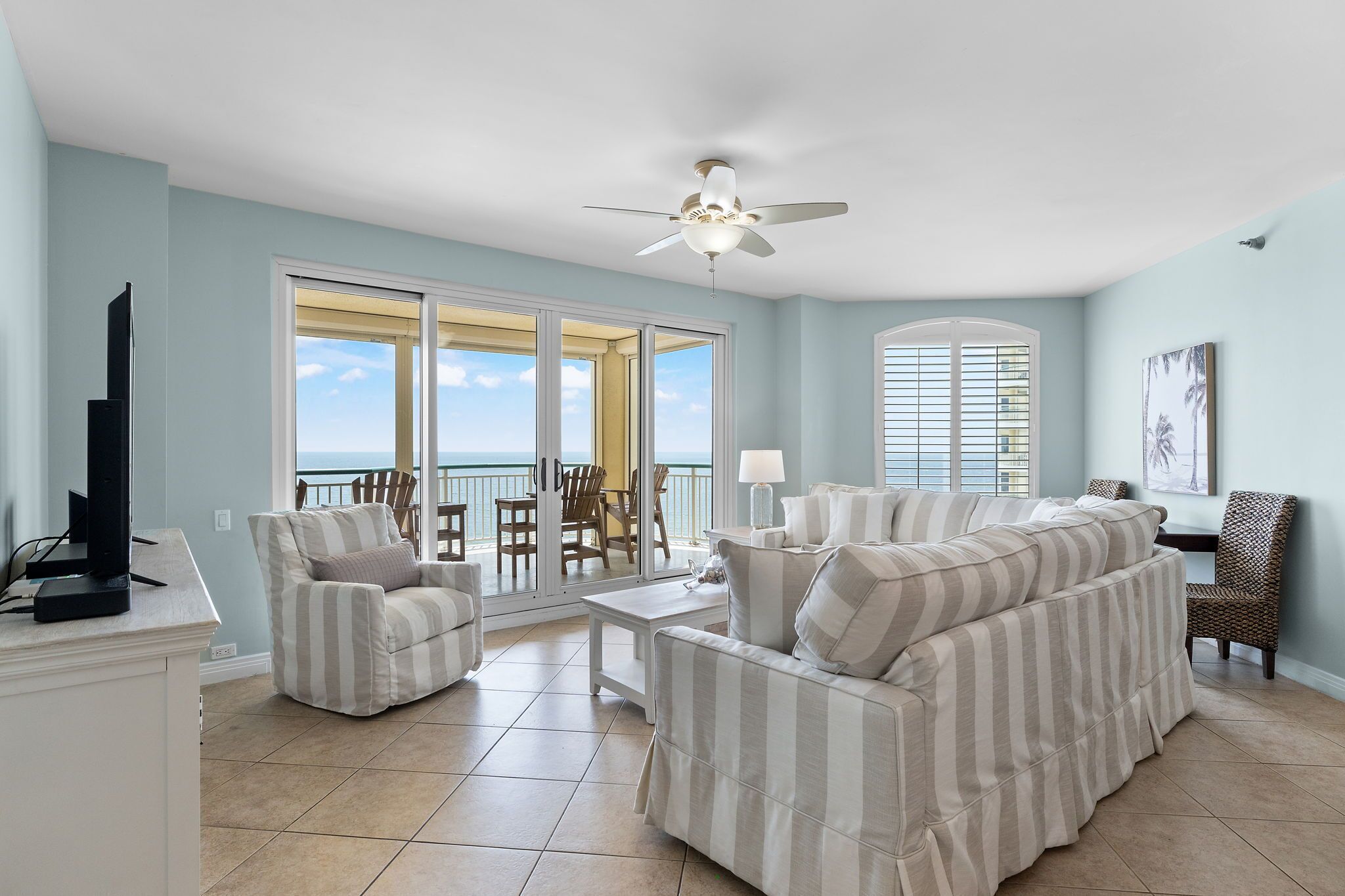 A living room with a sofa, chairs, a television, and a view of the ocean through large windows.