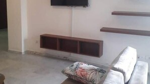 A living room with a grey sofa, a flat-screen TV mounted on the wall, and wooden shelves below. - house E. (Hammam Sousse)
