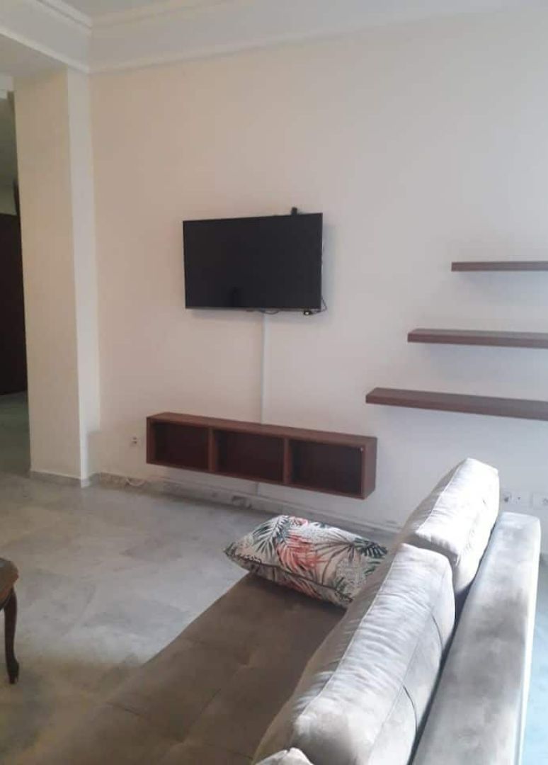 A living room with a sofa, a flat-screen TV mounted on the wall, and built-in shelves.