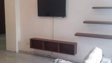 A living room with a sofa, a flat-screen TV mounted on the wall, and built-in shelves.