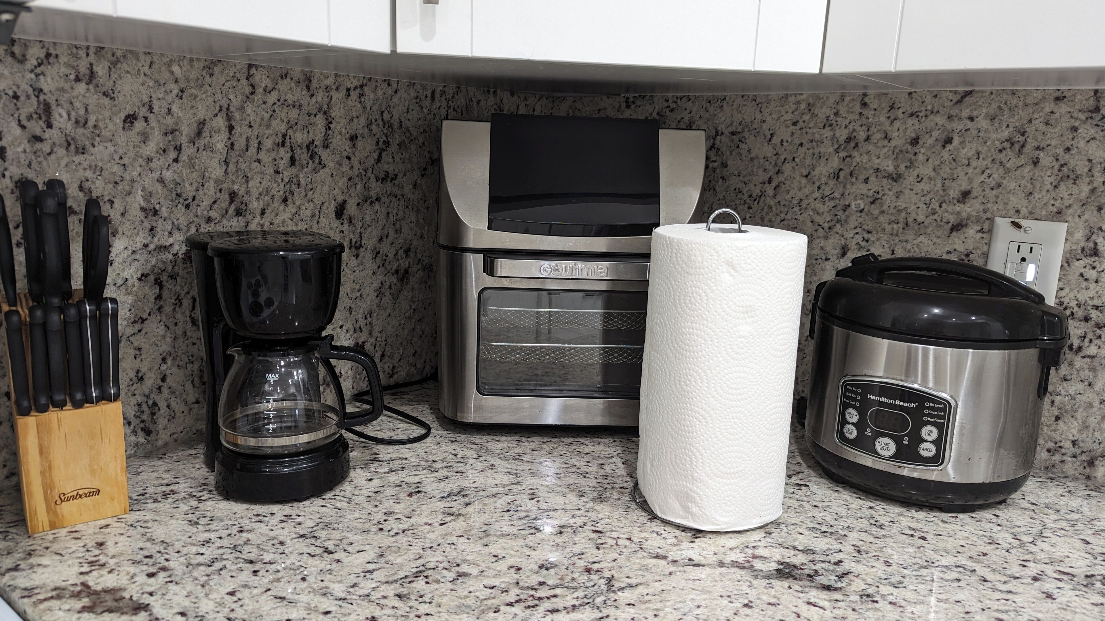 Un plan de travail de cuisine avec une machine à café, un porte-essuie-tout et une mijoteuse.