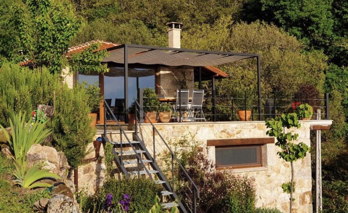 Una casa de piedra con un porche cubierto, mobiliario exterior y una escalera de piedra que lleva a la entrada.