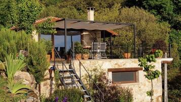 Una casa de piedra con un porche cubierto, mobiliario exterior y una escalera de piedra que lleva a la entrada.