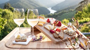 A picnic setup with cheese, fruits, and wine glasses on a wooden board, overlooking a valley.