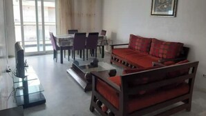 A living room with a red sofa, a coffee table, and a TV. There is a dining area with a table and chairs. - House F. (Hammam Sousse)