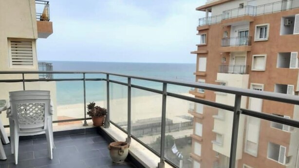 A balcony with a view of the sea, a chair, a potted plant, and a tiled floor. - House F. (Hammam Sousse)