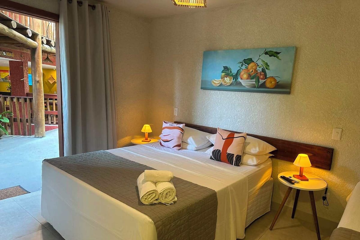 Una habitación de hotel con cama, almohadas, un cuadro, una mesita de noche y una lámpara.