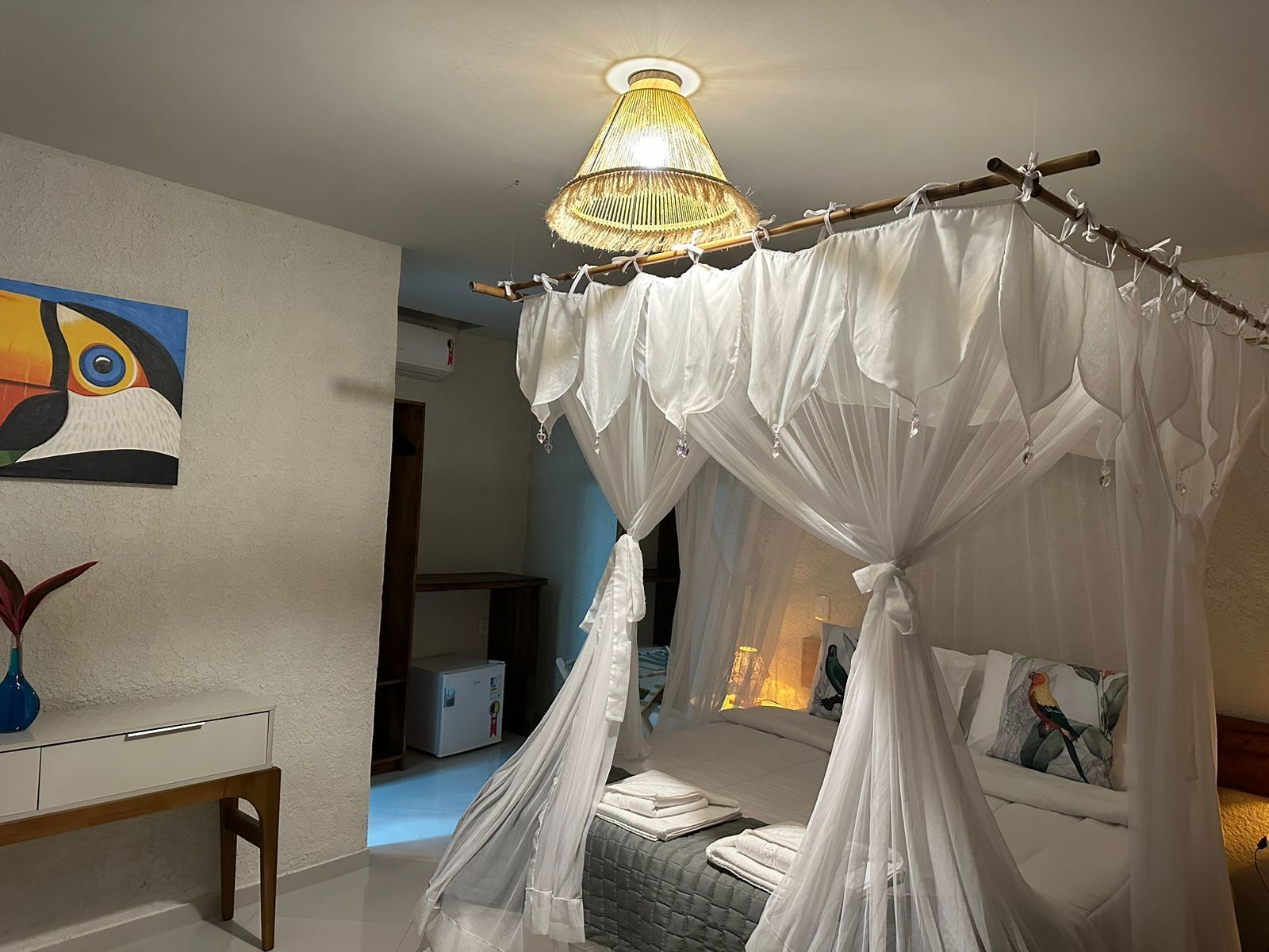 A bedroom with a canopy bed, a bedside table, a chair, and a painting on the wall.